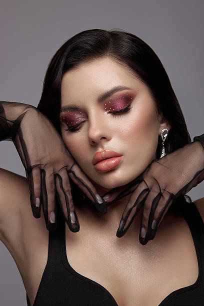 istock model poses with closed eyes, displaying striking makeup and intricate black gloves that enhance her graceful hands, exuding elegance and sophistication in a studio background 2223618086
