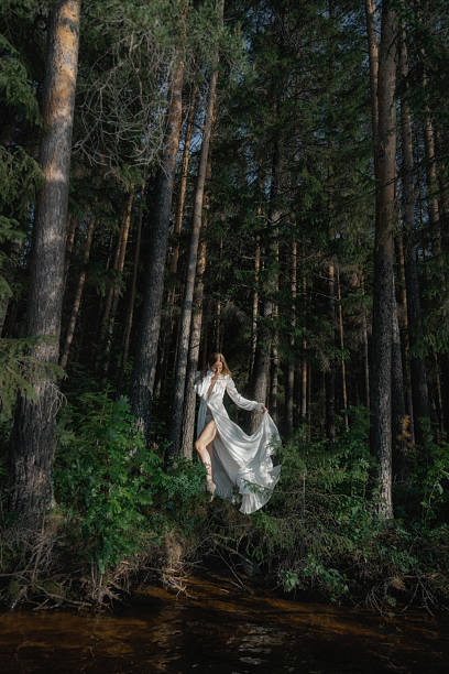 istock model elegantly stands in a flowing dress, surrounded by tall trees and lush greenery 2223618344