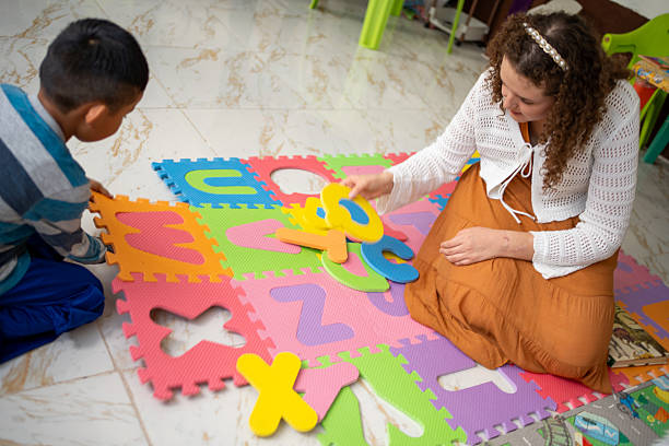 Preschool teacher and a young boy engaging in a playful learning activity, searching for letters on a colorful foam alphabet mat. Kindergarten early literacy, preschool education, hands-on learning
