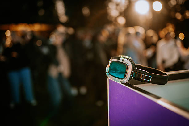 istock Close-up of a wireless silent disco headphone with a green light, placed on a corner stand, with a blurred background of people and bright stage lights. 2223629494