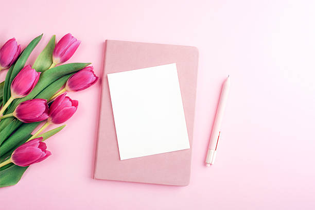 istock Blank white card with pink tulips, notebook and pen on pastel pink background. Top view, flat lay, mockup 2223636745