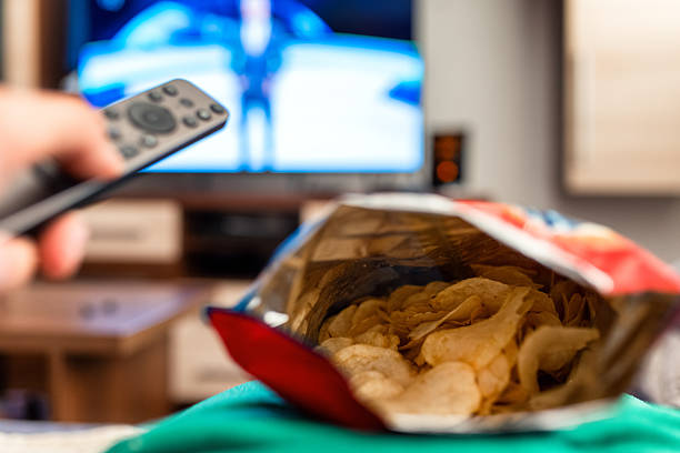 istock Switching chanels on tv with remote controller and package of chips in living room 2223637447