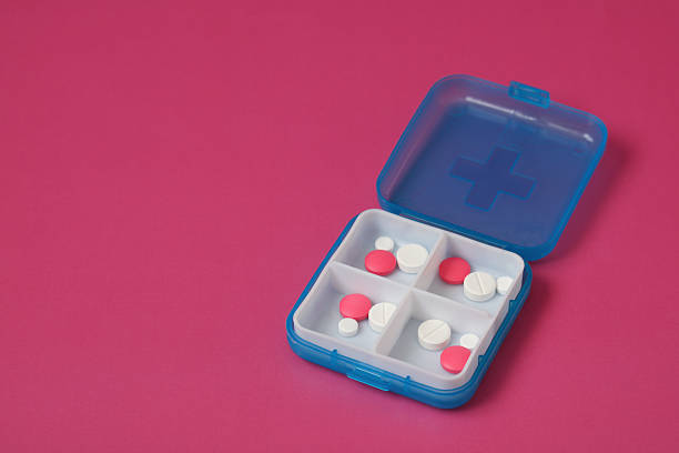 istock Blue pill organizer containing white and pink medicine on pink background 2223639617