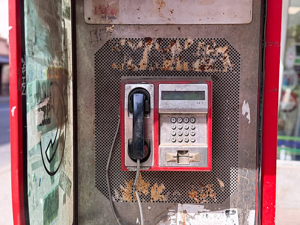 Old public payphone with keypad and receiver. Worn telephone booth with scratched metal panel and faded stickers.