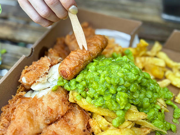 Close-up of a traditional British fish and chips meal served with mushy peas, tartar sauce, and fresh salad on a white plate in a restaurant.