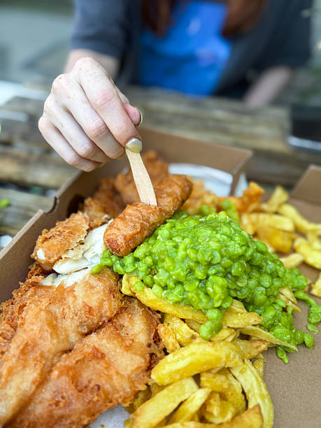 istock Image of traditional english fish supper, battered cod, chips, mushy peas served in takeaway cardboard box 2223644287