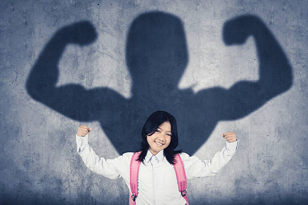 istock Confident schoolgirl with strong superhero shadow on the wall 2223650067