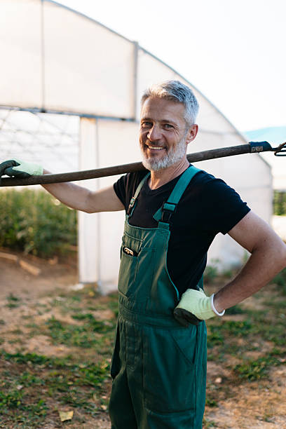 Farmer smiling and holding a pitchfork in a greenhouse