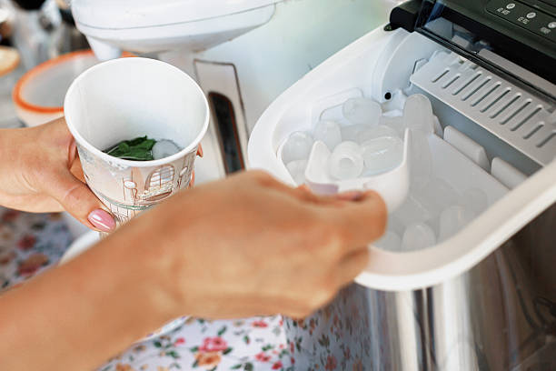 Close up of a woman's hands scooping ice from an ice maker into her cup containing a refreshing drink