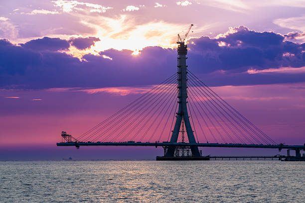 A dramatic and fiery sunset casts a vivid glow over the silhouette of the Danjiang Bridge under construction in Tamsui District New Taipei City Taiwan, enhancing the twilight scene.