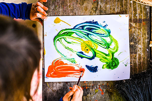 istock Child painting and doing an art project seen from above with paint and rustic found items in messy colorful outdoor space 2223684082