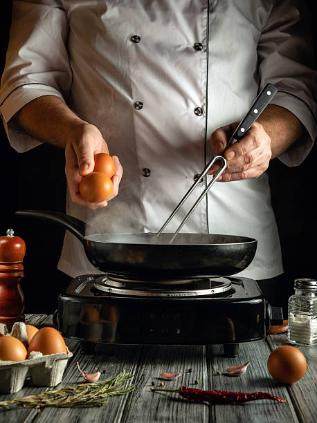 istock A chef performs meal prep by cracking fresh eggs into a frying pan on a stovetop. The rustic kitchen is filled with various cooking ingredients, emphasizing culinary creativity 2223685062