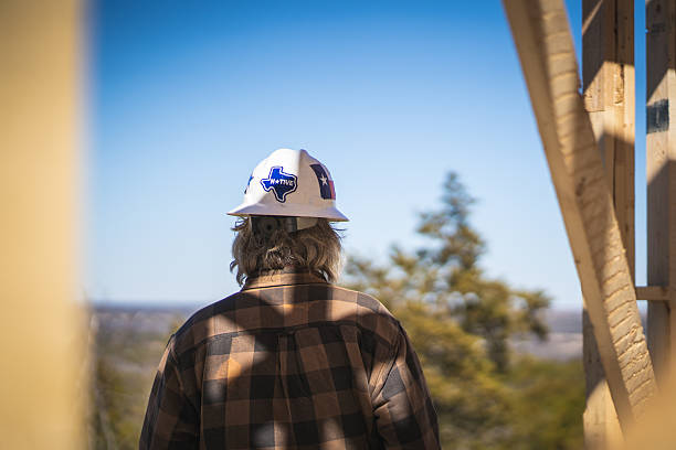 istock Construction Worker Wearing Hard Hat with Texas Flag Sticker Standing Inside of Wooden Frame of House at Construction Site and Looking Out at Scenic View 2223686450