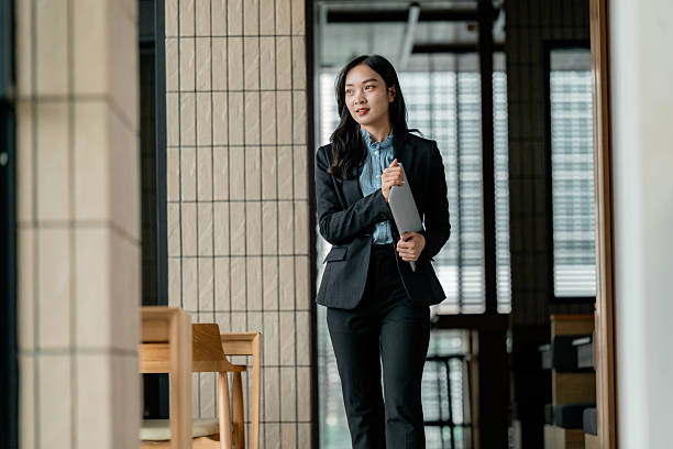 istock Young Asian businesswoman walking in a modern office while holding a tablet, looking confident and successful 2223687869
