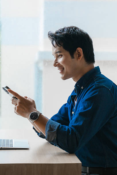 Professional male worker typing on smartphone, sitting at desk with laptop, expressing workplace satisfaction during workday