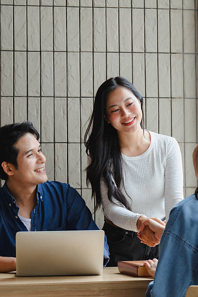 Professional Asian woman welcoming new team member, handshaking in bright modern office, signaling collaborative workplace environment