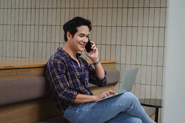 istock Young Asian freelancer talking on the phone and working on his laptop in a modern co-working space 2223689071