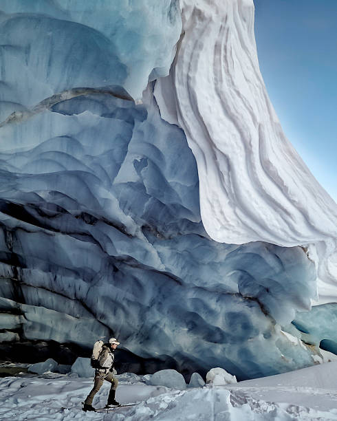 Ski mountaineer climbs below giant crevasse, glacier crevasses above him, Saas-Fee, Swiss Alps