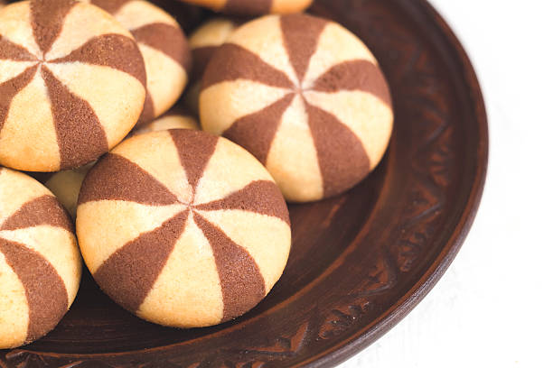Fresh two colored striped biscuits on a brown ceramic plate on a white background.