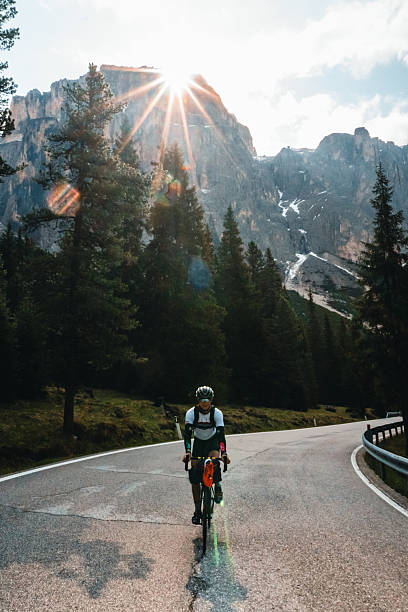 istock Young man rides bicycle on road through forest below mountains, Dolomites 2223694493