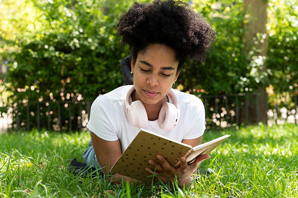 istock Woman reading a book while lying on grass in a park 2223696680
