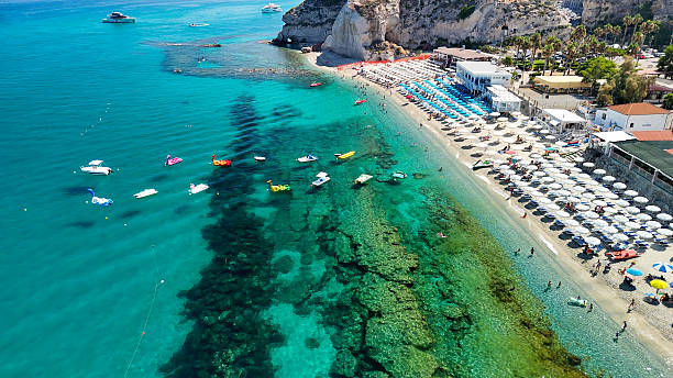 Tropea beach seen from above with sunbathers, umbrellas, and waves on a hot day.