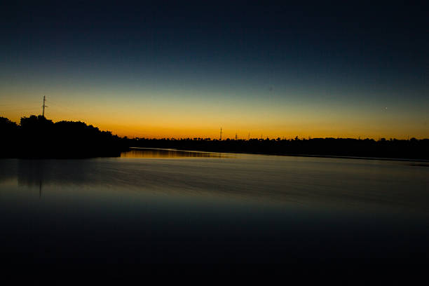 A body of water with trees in the back. Sky. Sunset. Nature. Sun. Clouds