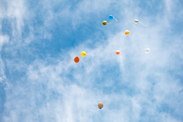 Colorful balloons rising in a blue sky with some clouds, representing celebration, freedom, and joy