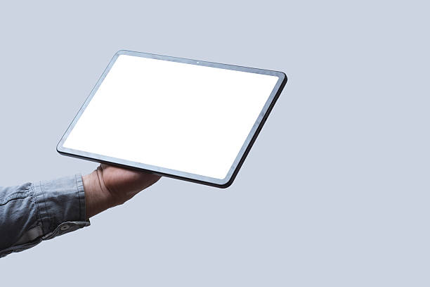 istock Close-up of a tablet with a blank white screen held in a man's hand against a neutral background. Mockup for showcasing web design, mobile apps, UI UX concepts and digital content. 2223730338