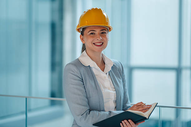 istock Smiling female architect wearing hardhat holding notebook in modern office building 2223734973