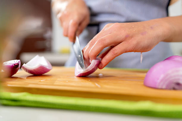 Close-up of a young chef meticulously slicing red onions, preparing ingredients for a peruvian ceviche dish in a small kitchen