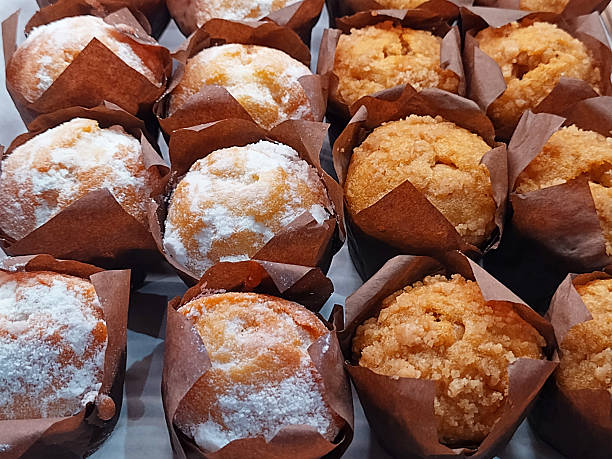 A tempting assortment of freshly baked muffins, some with a snowy powdered sugar dusting and others boasting a delightful crumbly topping