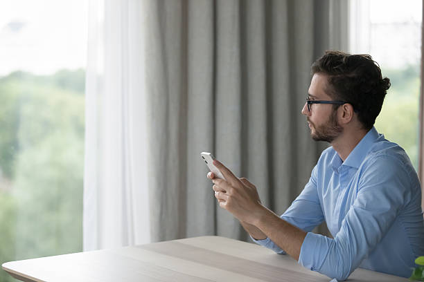 istock Pensive man sit at desk with smartphone staring out window 2223756707