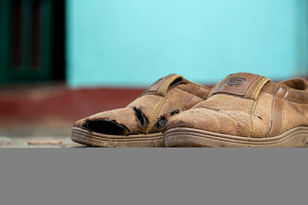 Close-up of worn brown shoes placed on dry, cracked earth, symbolizing hardship, resilience, and the everyday struggles of underprivileged village life in India.