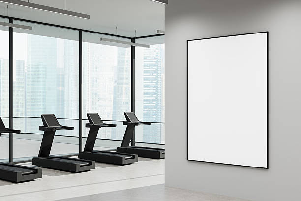 istock Modern gym interior with treadmills and large blank vertical poster frame on wall near window overlooking cityscape in daylight. 3D Rendering 2223762961