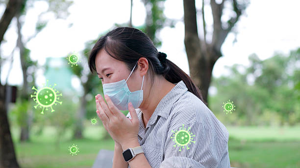 istock Asian woman wearing a protective mask, feeling sick and coughing outdoors, suffering from symptoms of a virus, flu, or severe PM2.5 air pollution while in a public park. 2223763245