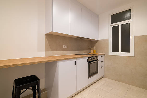 istock Modern kitchen side view with white cabinets, wood counter, oven and a single black bar stool 2223766117