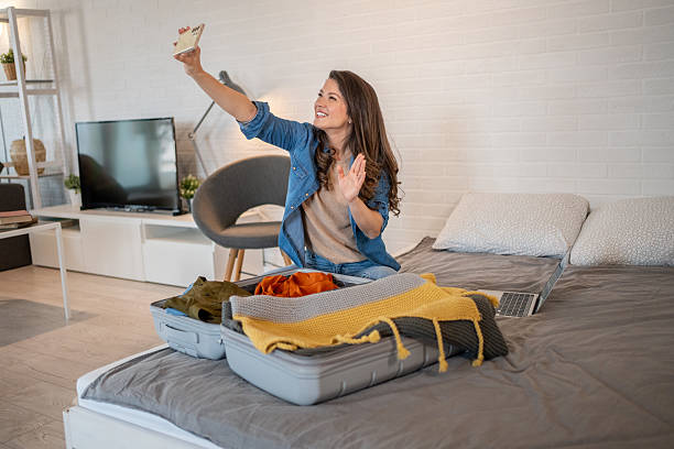 istock Young woman making video call while packing suitcase for travel 2223767906