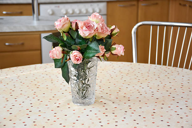 A macro photo of delicate pink rose blossoms in a glass vase placed on a light-colored table.