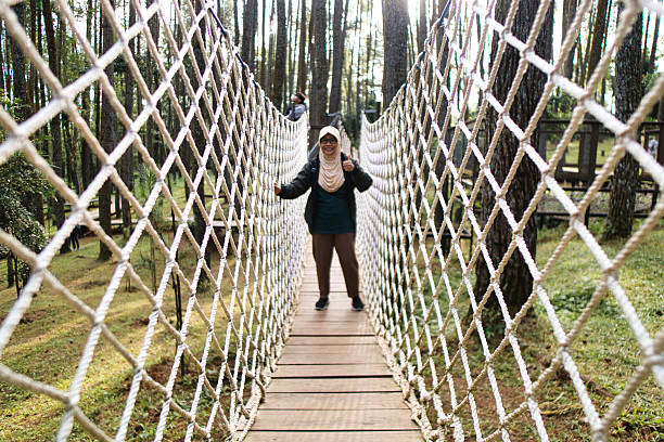 istock Woman Crossing Rope Bridge Surrounded by Forest Scenery in Daylight 2223769264