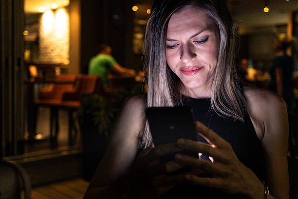 istock Beautiful blond woman sitting in a cafe at night while her face is illuminated by screen of her mobile phone. She is browsing social networks or internet for information. 2223772498