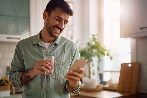 istock Happy man drinking smoothie while reading text message on cell phone at home. 2223786161