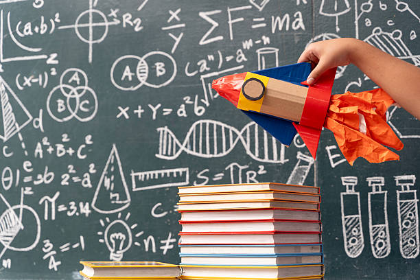 istock Child hand holding rocket over books with blackboard full of science and math formulas creative education concept 2223794844