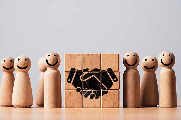 istock Wooden figures with smiling faces, symbolizing collaboration and teamwork, centered around a handshake icon on a cork circular base, representing partnership and mutual agreement. 2223800901
