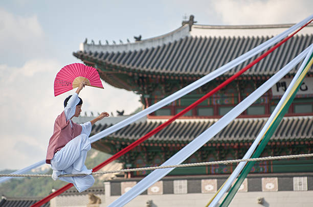 Seoul, South Korea - October 1, 2012: A male tightrope performer in traditional attire balances with a red fan as he entertains the audience in front of the historic Gwanghwamun Gate during the Chuseok Traditional Performing Arts Festival. The act is a classic part of Korean folk entertainment.
