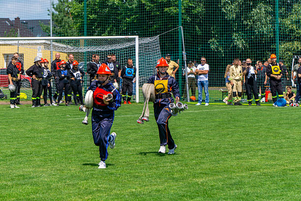 Sieroszewice, Greater Poland Voivodeship, Poland - june 29, 2025 Two female participants of a Youth Firefighting Team run across the field carrying rolled fire hoses and couplings. Wearing navy-blue athletic uniforms and red helmets, they compete in one of the firefighting events
