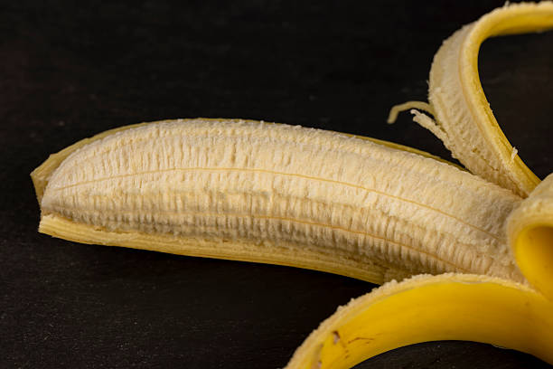 one open ripe yellow banana on a black slate board, ripe and sweet yellow banana on a kitchen board made of black stone