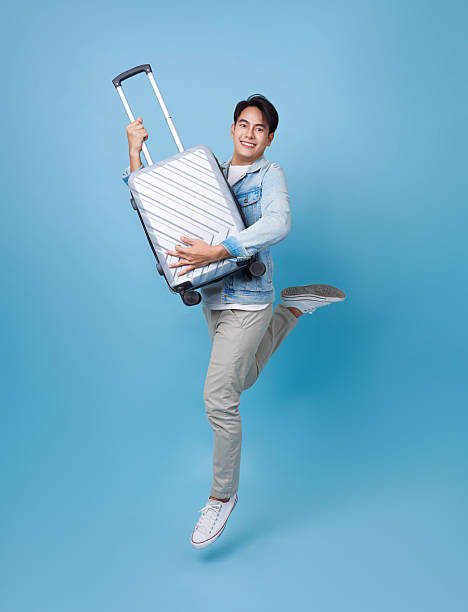 istock young excited asian man in a denim jacket jump energetically while holding suitcase isolated on blue background ready for his next adventure. 2223809982