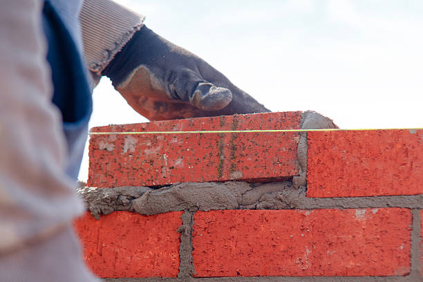 istock Close-up of skilled bricklayer working on construction site laying one more red brickin the wall 2223814355