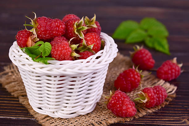 Fresh raspberries in a white basket on a dark wooden background.